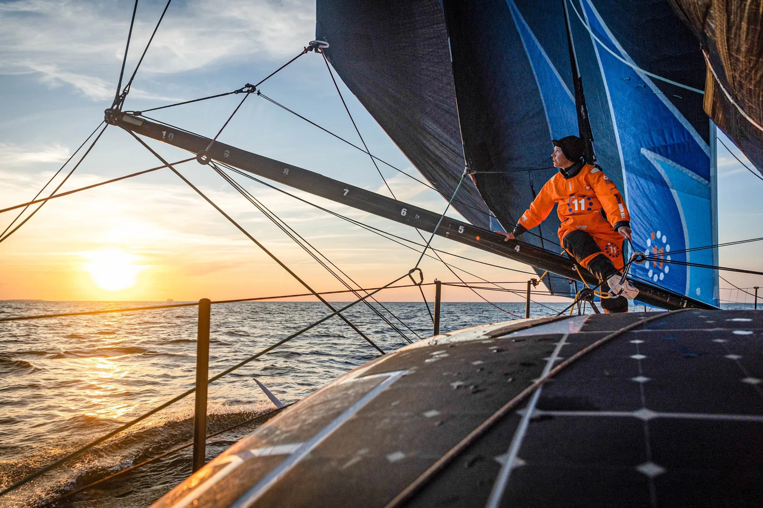 A crew member on the bow of an 11th Hour Racing yacht at sunset