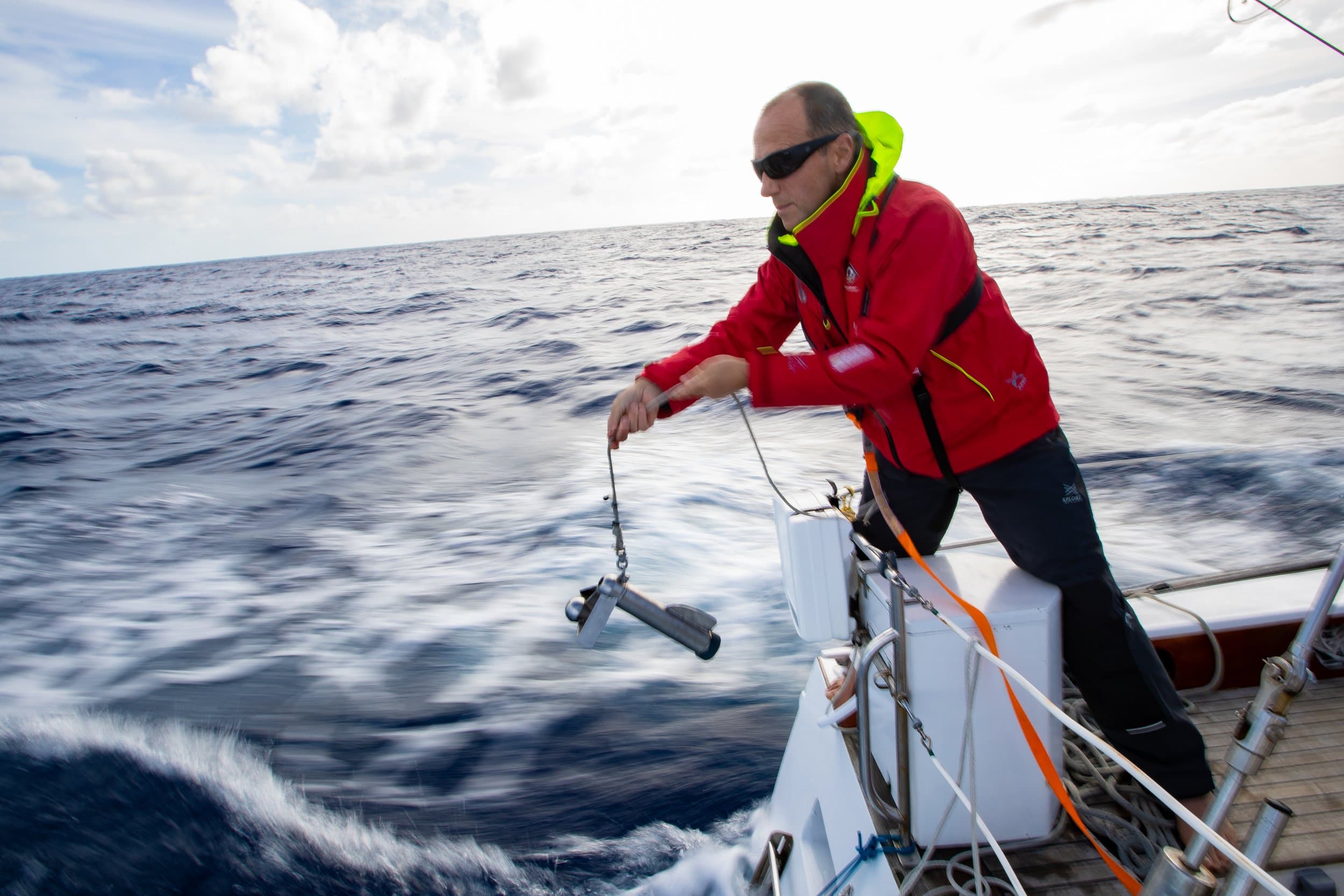A sailor lowering an eDNA sampling device off the stern of a yacht